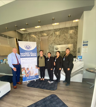 Sara Minnich, HRSA IEA, poses with David Phillips, Director of Community Development and PR (left) and the Medical Assistant team in the new building.