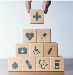 A stock image of a person building a block pyramid. The blocks depict different icons associated with the medical field.