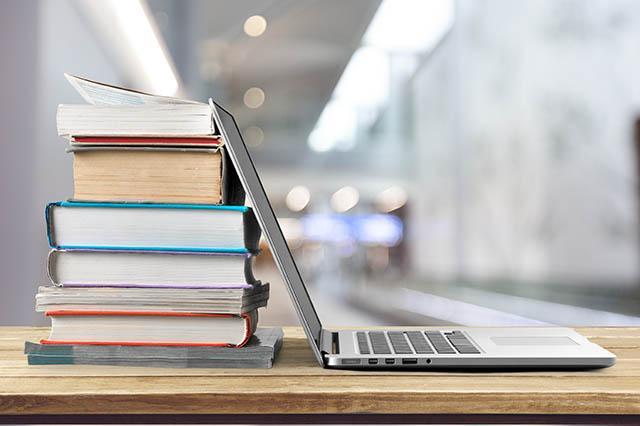 A laptop and a stack of books are sitting on a desk.